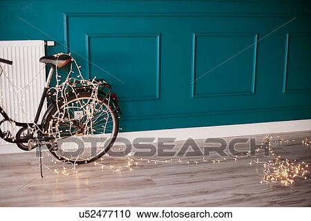 Stock Image - Bicycle leaning against wall, indoors, decorated with fairy lights. Fotosearch