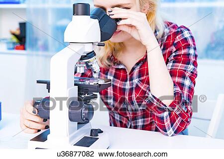 Stock Image - Biology lesson. Student using a light microscope.. Fotosearch