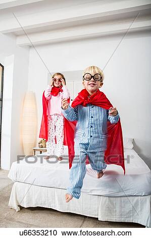 Stock Image - Boy and female twin in red capes jumping from bed. Fotosearch