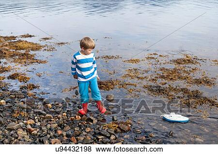 Stock Photo - Boy at fjord water's edge playing with toy boat, Aure, More og Romsdal, Norway. Fotosearch