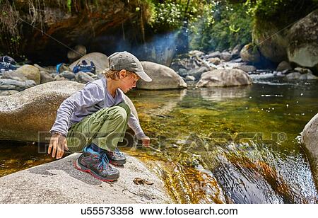 Stock Photo - Boy crouching on rock beside water pool, Ventilla, La Paz, Bolivia, South America. Fotosearch