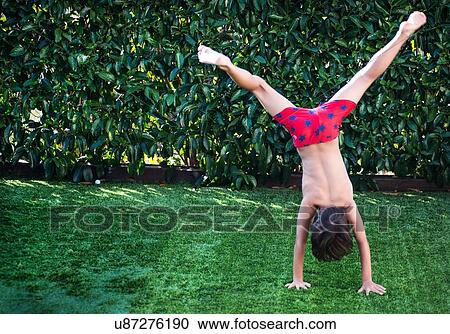 Stock Image - Boy doing handstand on grass. Fotosearch