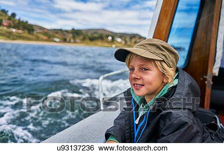 Stock Photograph - Boy looking out from motor boat at sea, Puno, Peru. Fotosearch