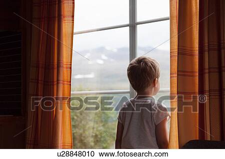 Stock Image - Boy looking through curtained window. Fotosearch