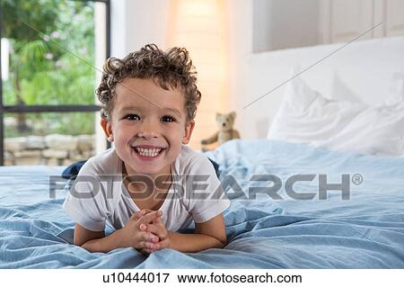 Boy lying on front on bed View Large Photo Image Stock Photo - Boy lying on front on bed. Fotosearch