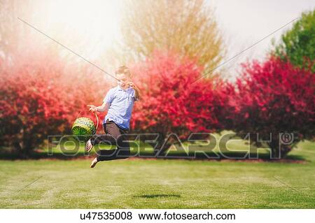 Stock Photo - Boy outdoors, jumping in air, holding Easter basket. Fotosearch