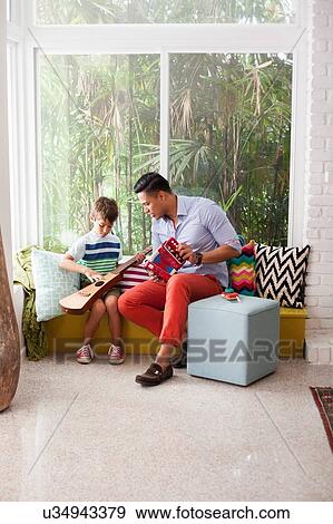 Stock Photo - Boy playing guitar with music teacher on window seat. Fotosearch