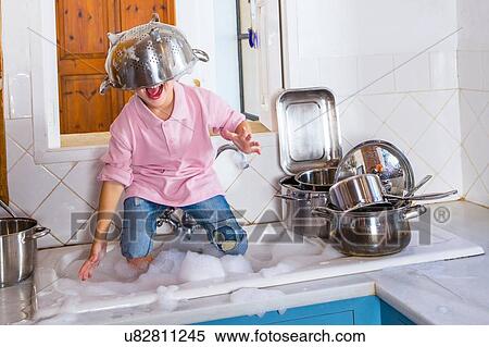 Stock Photography - Boy playing in kitchen sink with colander on his head. Fotosearch
