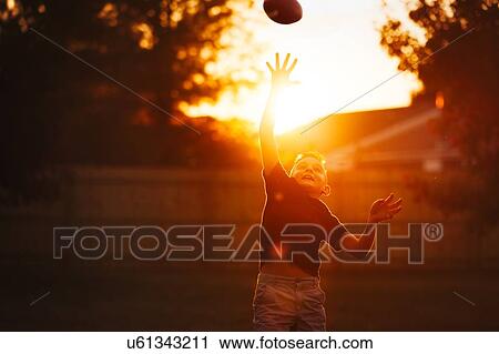 Boy practicing american football in garden reaching to catch ball mid air at sunset View Large Photo Image Stock Image - Boy practicing american football in garden reaching to catch ball mid air at sunset. Fotosearch