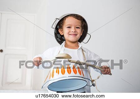 Stock Image - Boy pretending to be drummer using kitchen pots and utensils. Fotosearch