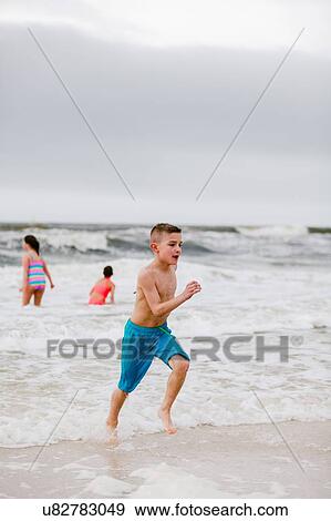 Stock Photo - Boy running along water's edge at beach, Dauphin Island, Alabama, USA. Fotosearch