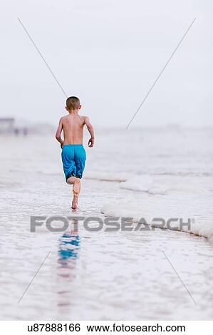 Stock Photograph - Boy running along water's edge at beach, rear view, Dauphin Island, Alabama, USA. Fotosearch