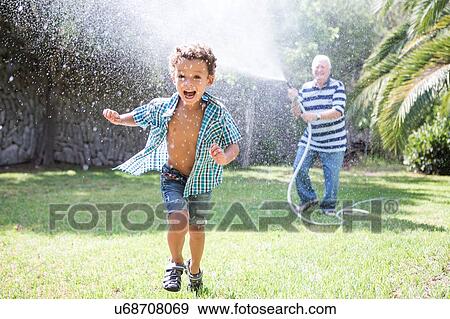 Boy running away from grandfather spraying hosepipe in garden View Large Photo Image Stock Photo - Boy running away from grandfather spraying hosepipe in garden. Fotosearch