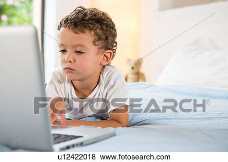 Boy using laptop on bed View Large Photo Image Stock Photo - Boy using laptop on bed. Fotosearch