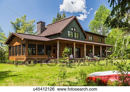 Stock Photograph - Brown and green stained spruce wood country home with veranda, Quebec, Canada. Fotosearch