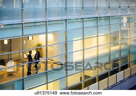 Stock Photo - Businessman and businesswoman having discussion by window. Fotosearch