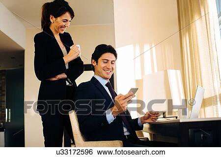 Stock Photograph - Businessman and businesswoman sharing text message in hotel room. Fotosearch