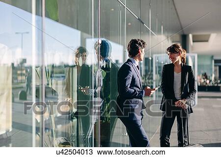 Stock Image - Businessman and businesswoman talking outside glass building, Malpensa, Milan. Fotosearch