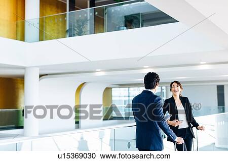 Stock Image - Businessman and businesswoman with wheeled luggage in hotel building. Fotosearch