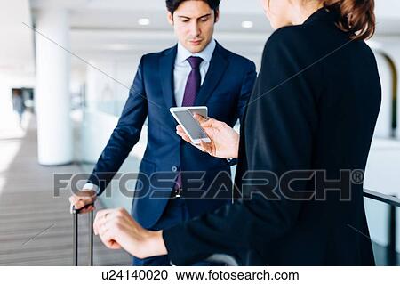 Stock Image - Businessman and businesswoman with wheeled luggage in hotel building. Fotosearch