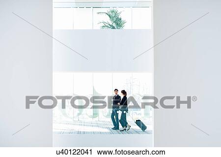 Stock Image - Businessman and businesswoman with wheeled luggage in hotel building. Fotosearch