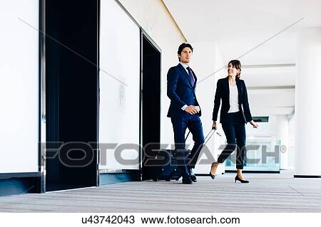 Businessman and businesswoman with wheeled luggage in hotel building View Large Photo Image Stock Image - Businessman and businesswoman with wheeled luggage in hotel building. Fotosearch