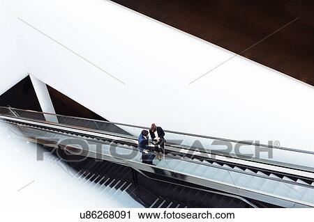 Businessman and businesswoman with wheeled luggage on escalator in hotel building View Large Photo Image Stock Image - Businessman and businesswoman with wheeled luggage on escalator in hotel building. Fotosearch