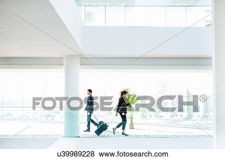 Businessman and businesswoman with wheeled luggage in hotel building View Large Photo Image Stock Photo - Businessman and businesswoman with wheeled luggage in hotel building. Fotosearch