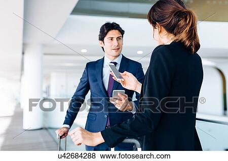 Stock Photo - Businessman and businesswoman with wheeled luggage in hotel building. Fotosearch