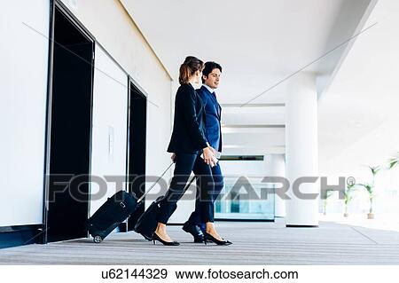 Businessman and businesswoman with wheeled luggage exiting hotel escalators View Large Photo Image Stock Photo - Businessman and businesswoman with wheeled luggage exiting hotel escalators. Fotosearch