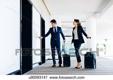Businessman and businesswoman with wheeled luggage waiting for hotel escalators View Large Photo Image Stock Photo - Businessman and businesswoman with wheeled luggage waiting for hotel escalators. Fotosearch