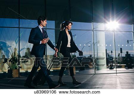 Businessman and businesswoman with wheeled luggage passing glass building, Malpensa, Milan View Large Photo Image Stock Photograph - Businessman and businesswoman with wheeled luggage passing glass building, Malpensa, Milan. Fotosearch