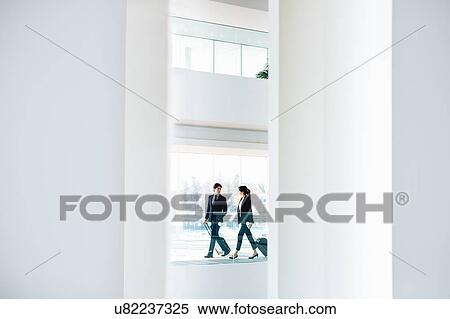 Stock Photography - Businessman and businesswoman with wheeled luggage in hotel building. Fotosearch