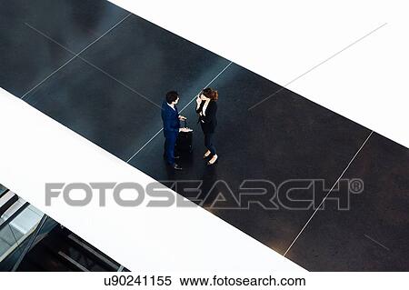 Stock Photography - Businessman and businesswoman with wheeled luggage in hotel building. Fotosearch