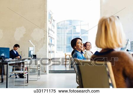 Stock Photography - Businessman and businesswomen sitting in office, women sitting in a row, laughing. Fotosearch