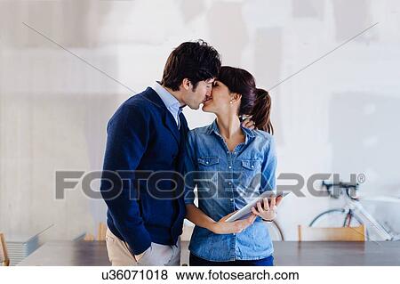 Stock Photo - Businessman and woman in office, kissing, woman holding digital tablet. Fotosearch