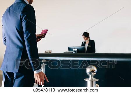 Stock Image - Businessman checking in at hotel reception. Fotosearch