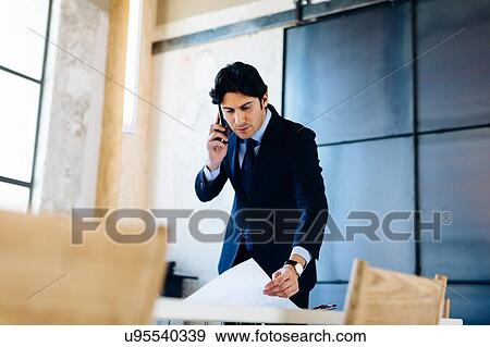 Businessman in office, using smartphone, looking through documents View Large Photo Image Stock Photo - Businessman in office, using smartphone, looking through documents. Fotosearch