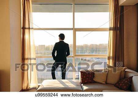 Picture - Businessman looking out of hotel bedroom window. Fotosearch