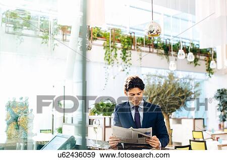 Stock Photo - Businessman reading the newspapers while having drink at bar. Fotosearch