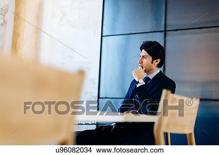 Businessman sitting at desk, thoughtful expression View Large Photo Image Picture - Businessman sitting at desk, thoughtful expression. Fotosearch