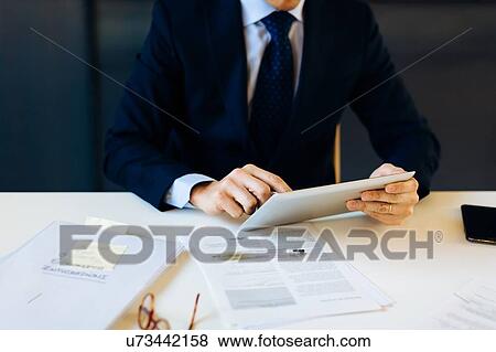 Businessman sitting at desk, using digital tablet, mid section View Large Photo Image Stock Photo - Businessman sitting at desk, using digital tablet, mid section. Fotosearch
