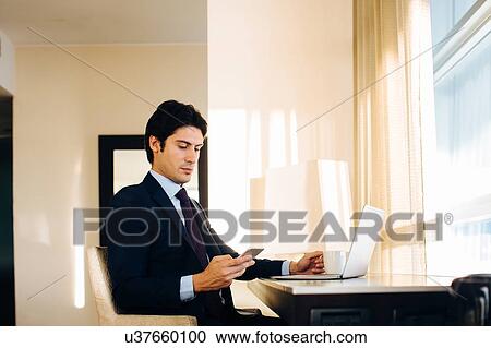 Businessman texting while using laptop by hotel room window View Large Photo Image Stock Image - Businessman texting while using laptop by hotel room window. Fotosearch
