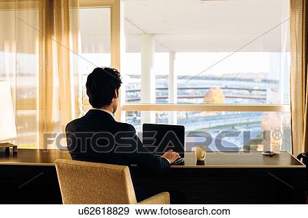 Businessman using laptop and looking out of hotel bedroom window View Large Photo Image Stock Photo - Businessman using laptop and looking out of hotel bedroom window. Fotosearch