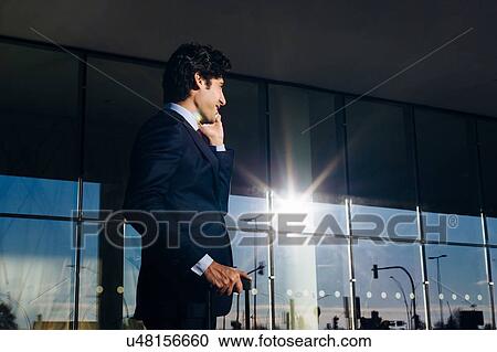 Stock Image - Businessman using mobile phone outside glass building, Malpensa, Milan. Fotosearch