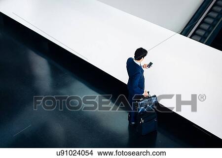 Picture - Businessman with wheeled luggage in hotel building. Fotosearch