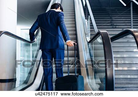 Businessman with wheeled luggage on hotel escalator View Large Photo Image Stock Photo - Businessman with wheeled luggage on hotel escalator. Fotosearch