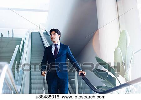 Businessman with wheeled luggage on hotel escalator View Large Photo Image Stock Photograph - Businessman with wheeled luggage on hotel escalator. Fotosearch