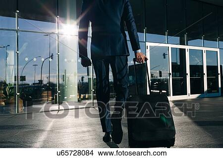 Picture - Businessman with wheeled luggage passing glass building, Malpensa, Milan. Fotosearch