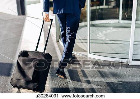 Businessman with wheeled luggage entering revolving doors of building View Large Photo Image Stock Image - Businessman with wheeled luggage entering revolving doors of building. Fotosearch